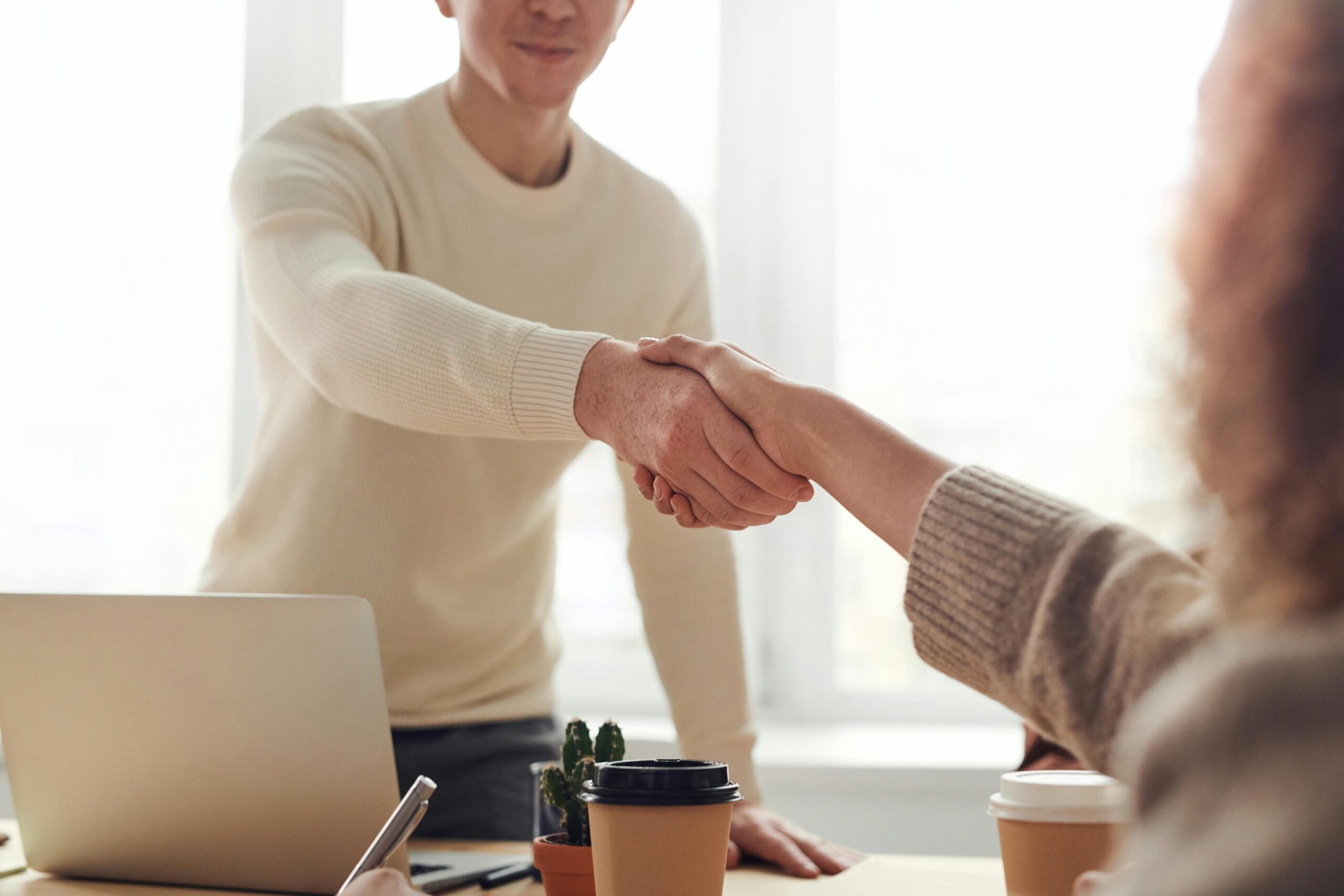two adults shaking hands over a desk to celebrate completing a deal